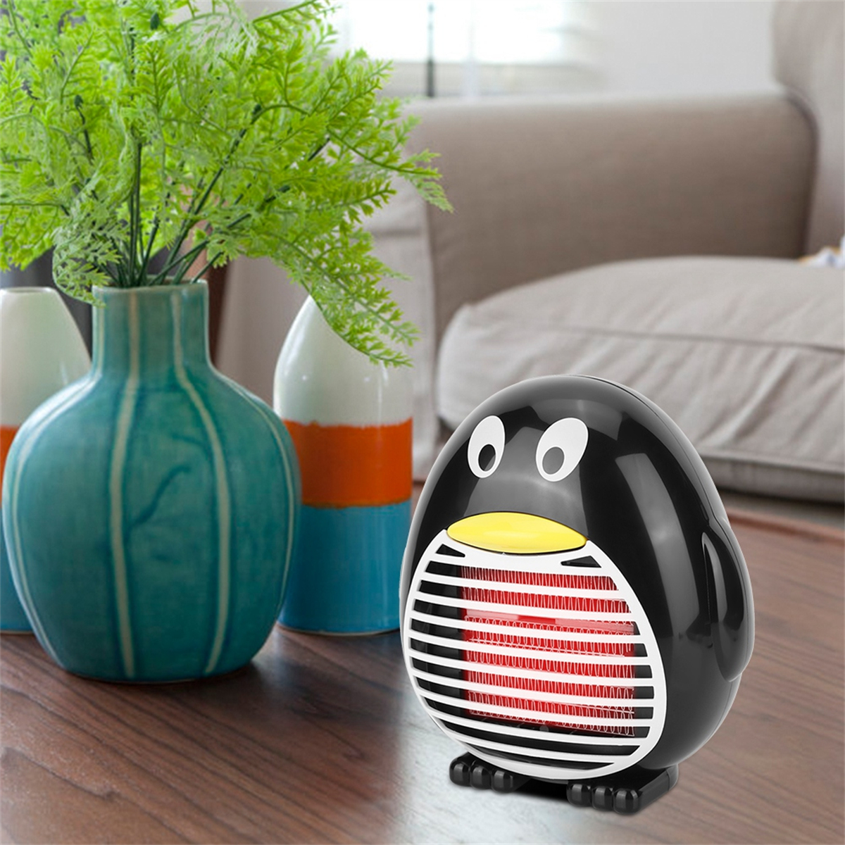 Ein schwarzer pinguinförmiger Heizlüfter mit einem roten Heizelement, neben einer türkisfarbenen Vase und einer Pflanze.