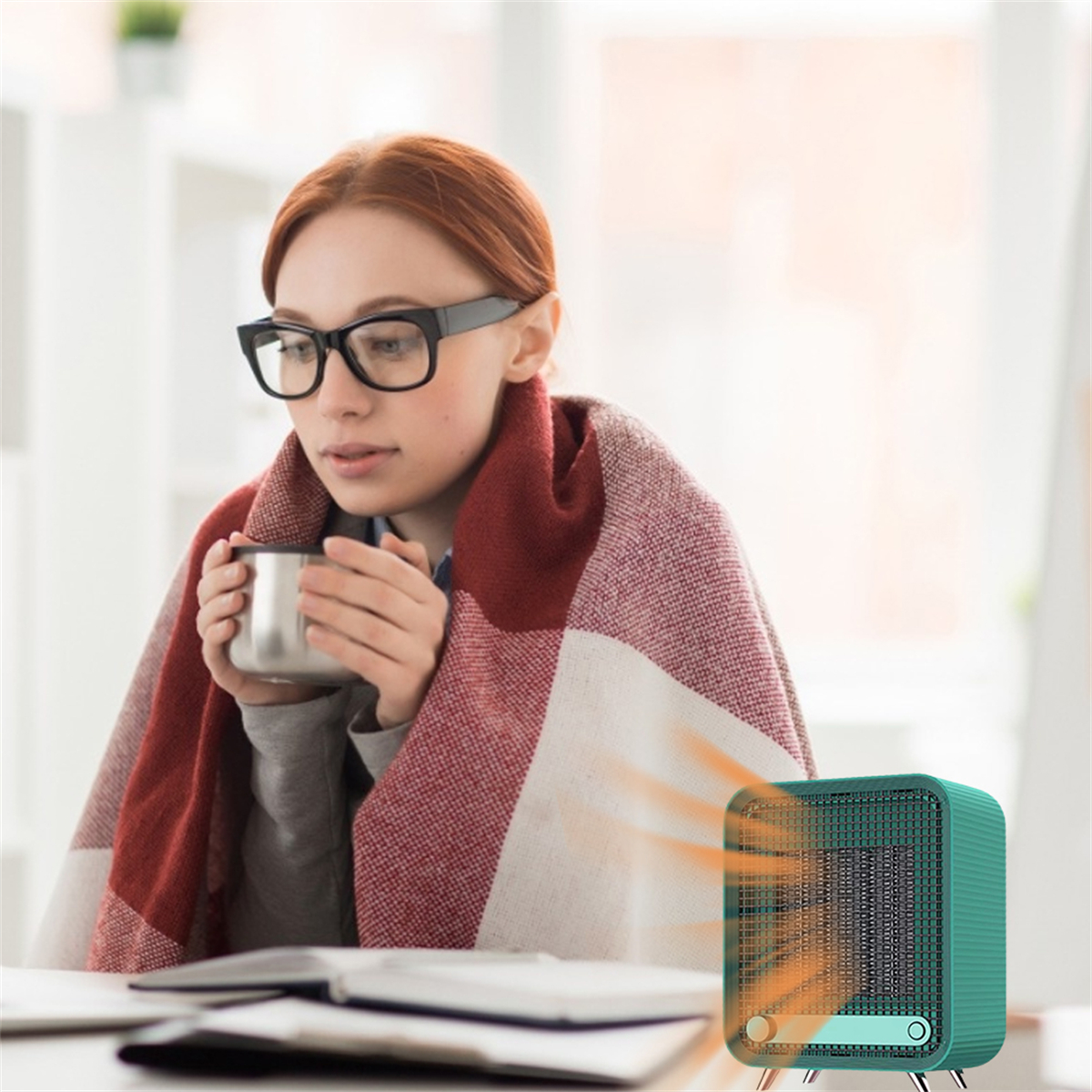 Frau in Decke, hält eine Tasse, mit einem kleinen teal Heizgerät in einer Raumeinstellung.