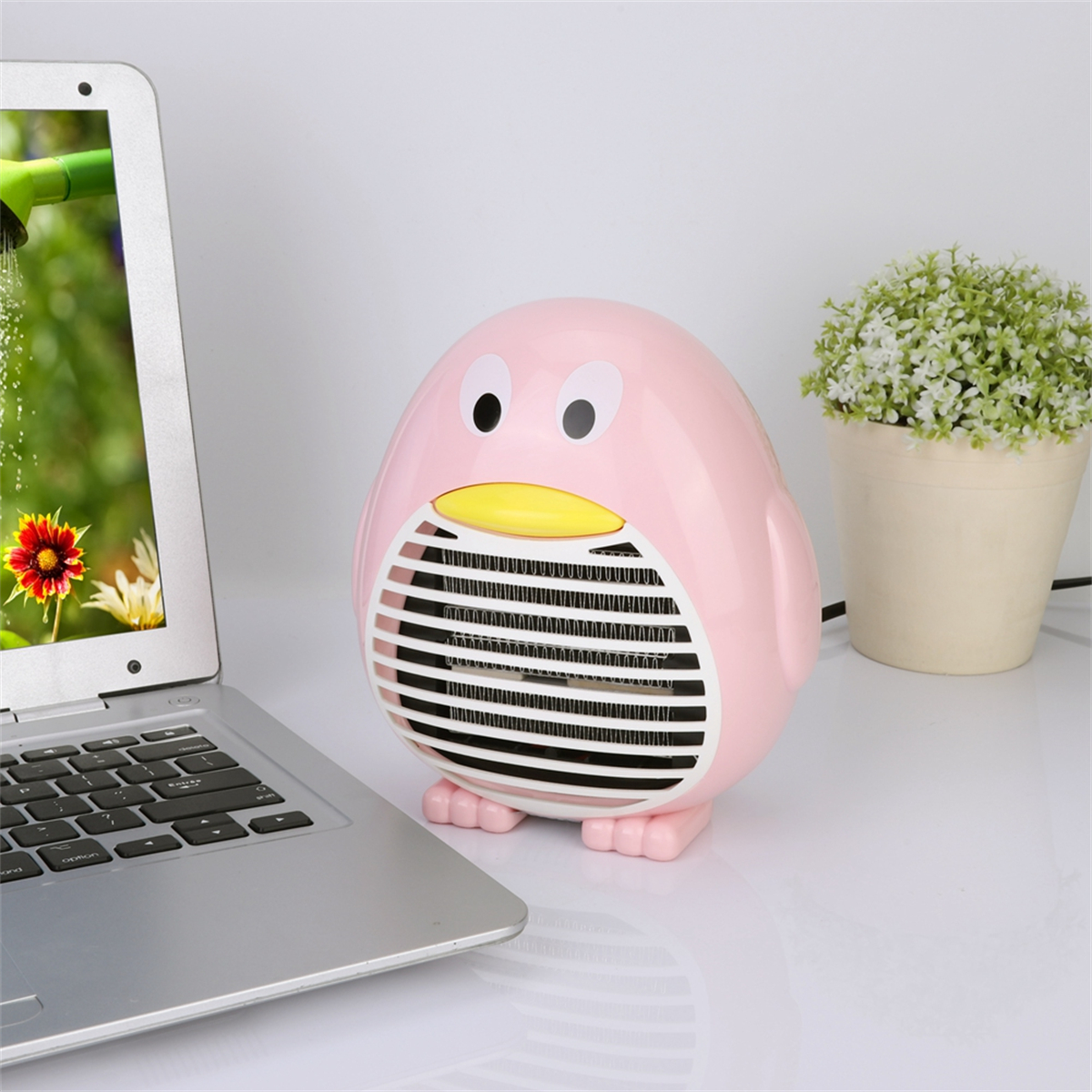 Ein rosa pinguinförmiger Heizlüfter neben einem Laptop und einer Pflanze.