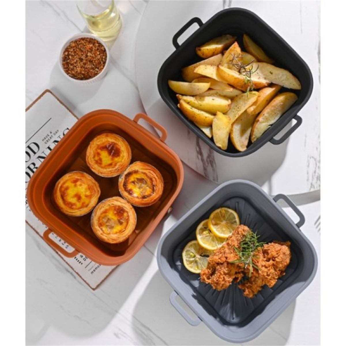 Drei quadratische Behälter mit Essen: Bratkartoffeln, Eiertörtchen und gebratenes Hühnchen mit Zitronenscheiben.