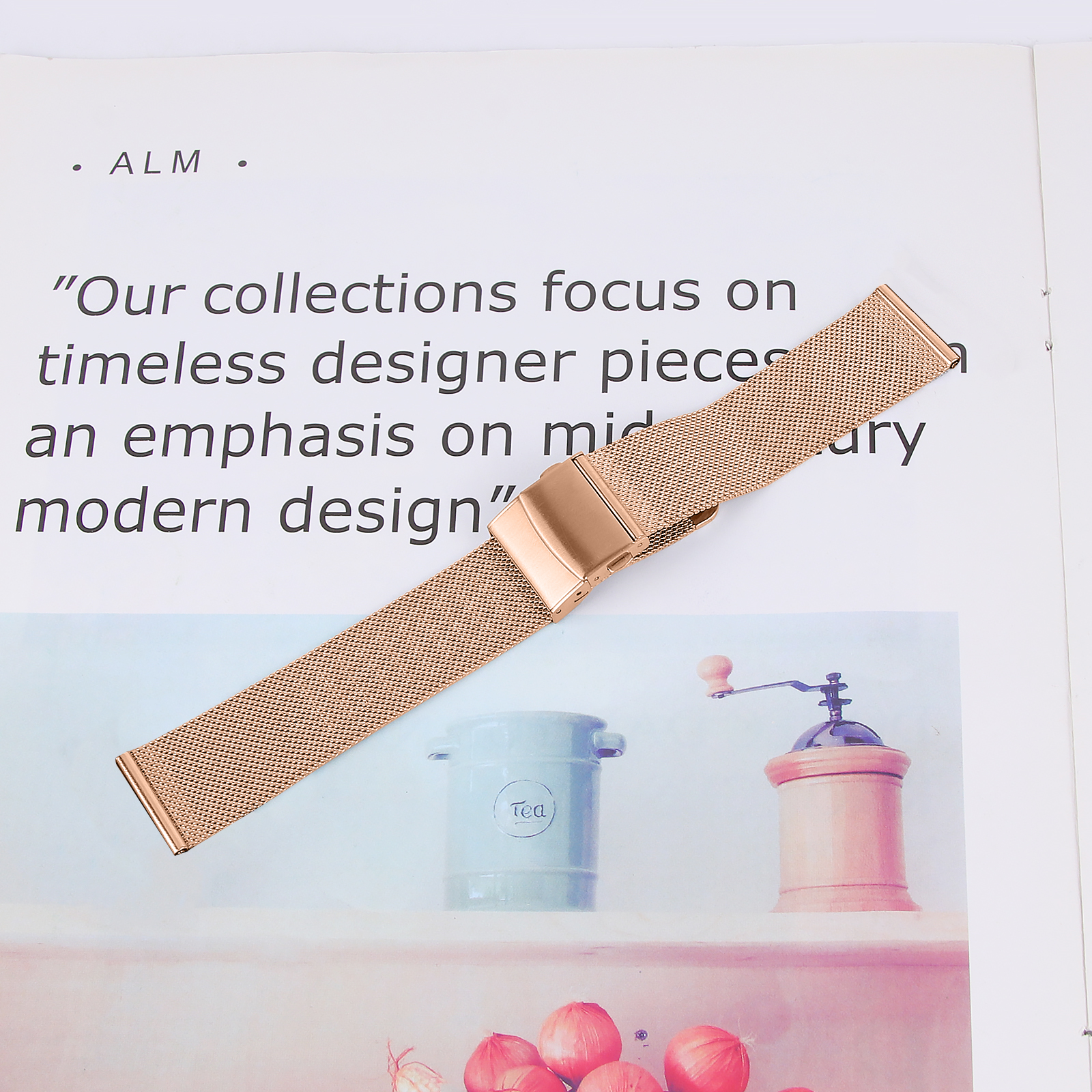 Pasek do zegarka w kolorze różowego złota na białym papierze. Pasek jest siatkowy z zapięciem.