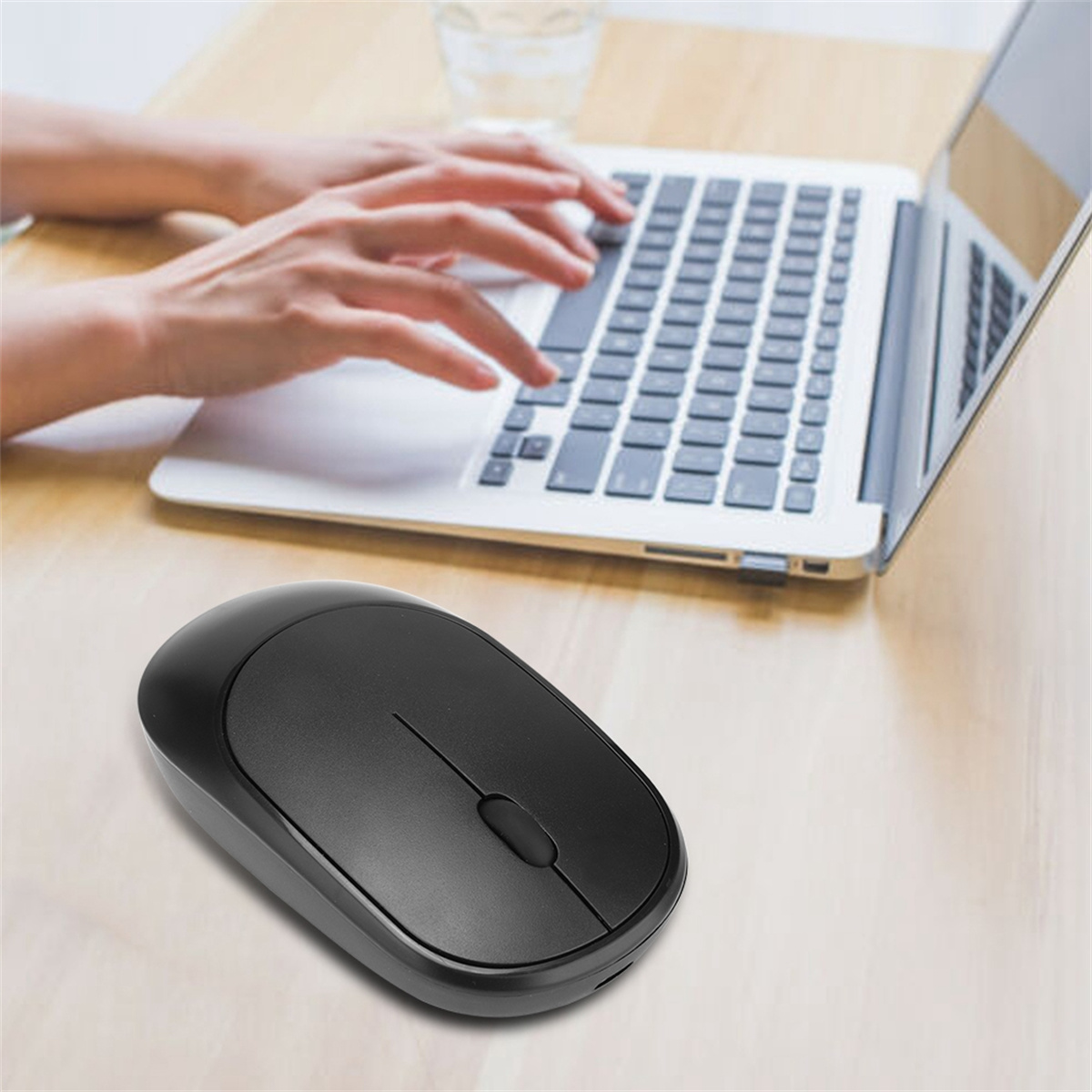 Die Hände einer Person, die einen Laptop benutzt, und eine schwarze kabellose Maus auf einem Holztisch.