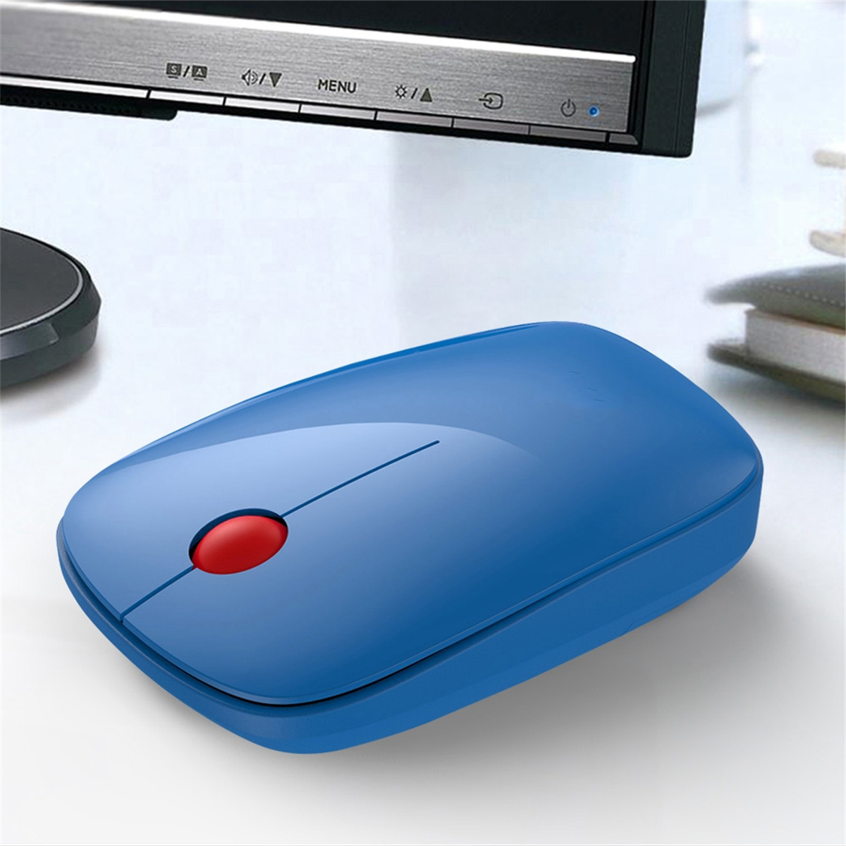 Blaue drahtlose Maus mit roter Taste auf weißem Schreibtisch. Im Hintergrund ist ein Monitor.