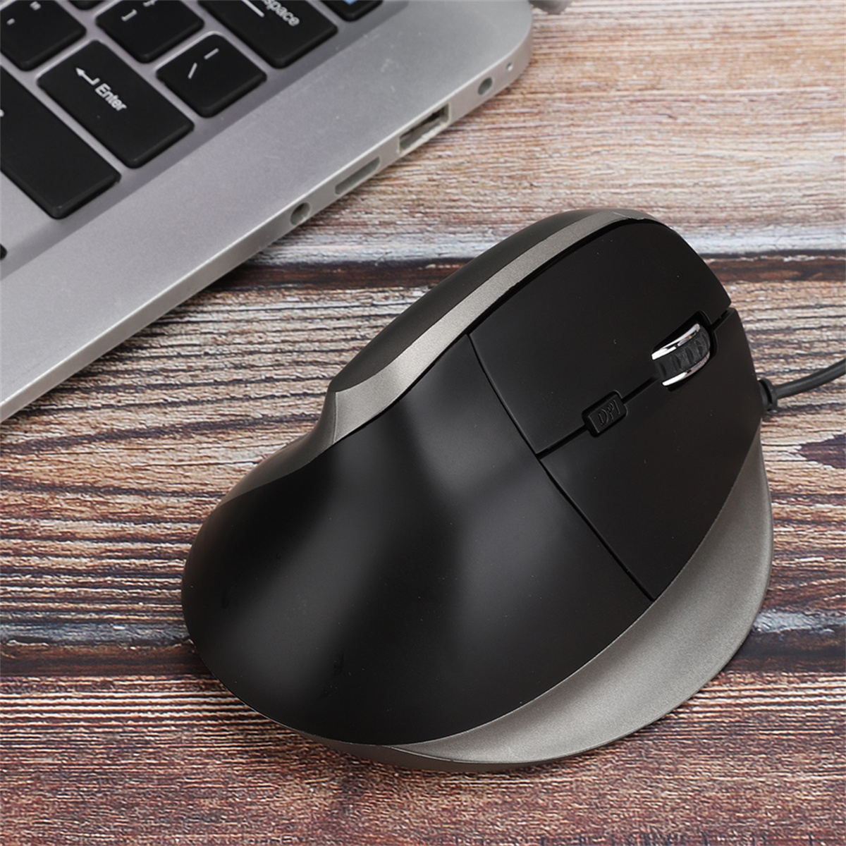 Eine ergonomische Maus in Schwarz und Grau, die auf einem Holztisch in der Nähe einer Laptop-Tastatur liegt.