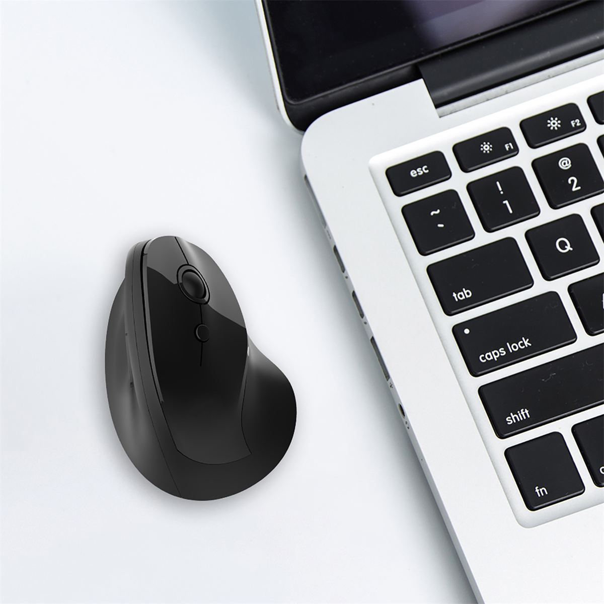 Schwarze ergonomische Maus neben einer Laptop-Tastatur auf weißer Oberfläche.