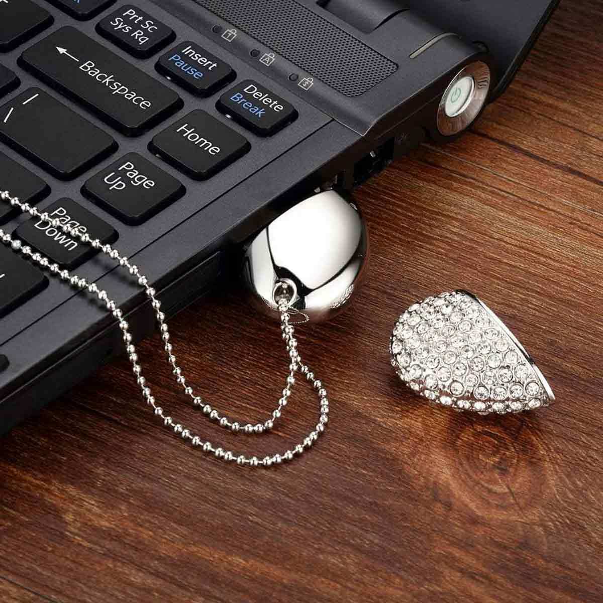 Eine Laptop-Tastatur mit einem silbernen USB-Stick und einer Anhänger-Halskette auf Holzoberfläche.