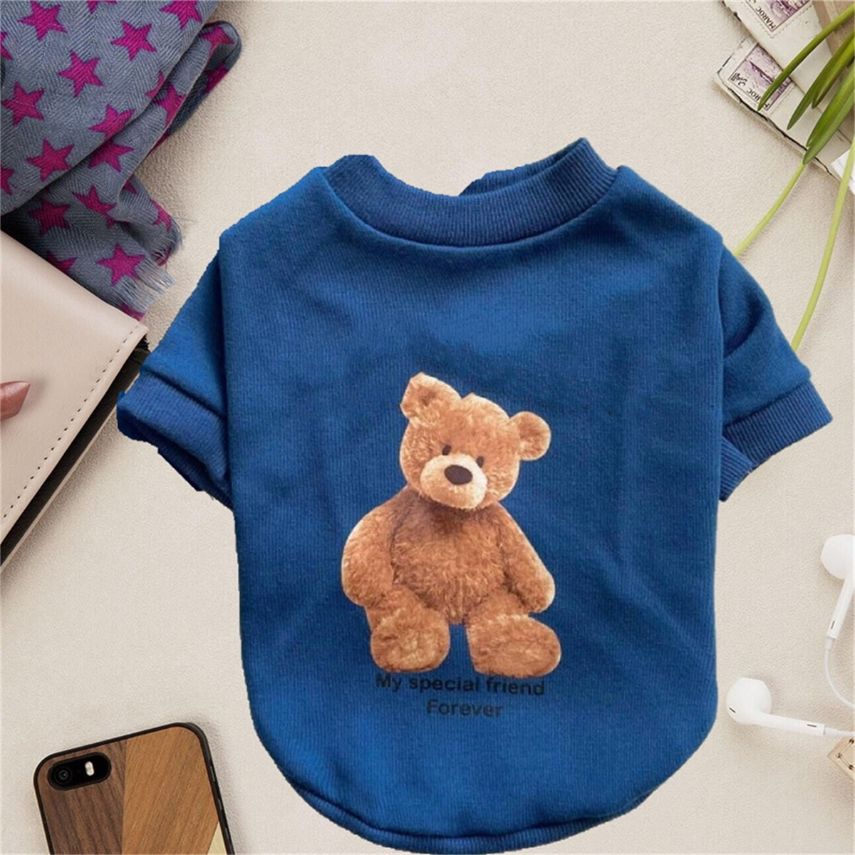 Blaues Hunde-Shirt mit Teddybär-Motiv und Text. Verschiedene Gegenstände drumherum.