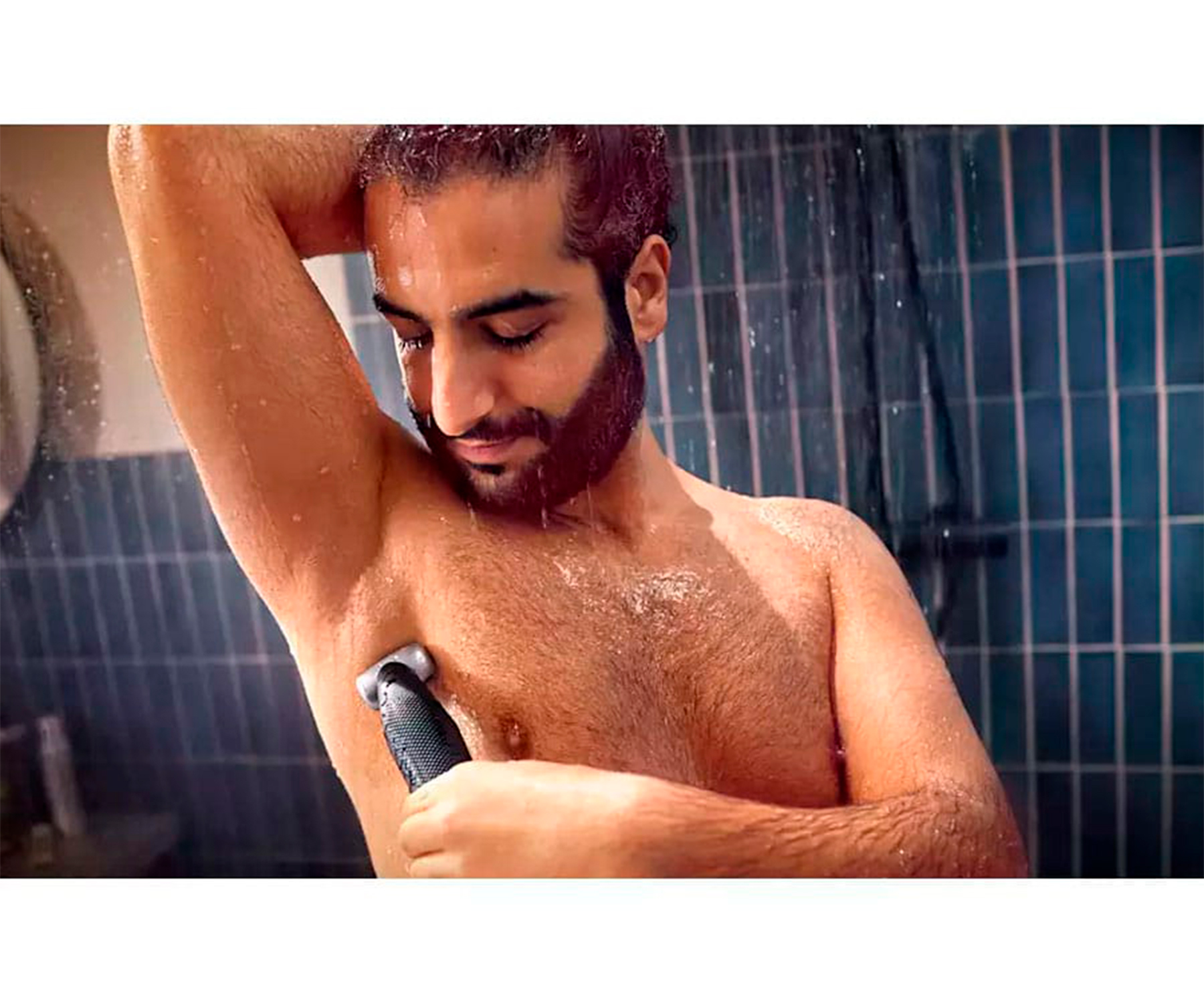 Hombre afeitándose la axila con recortador en la ducha. Gotas de agua visibles.