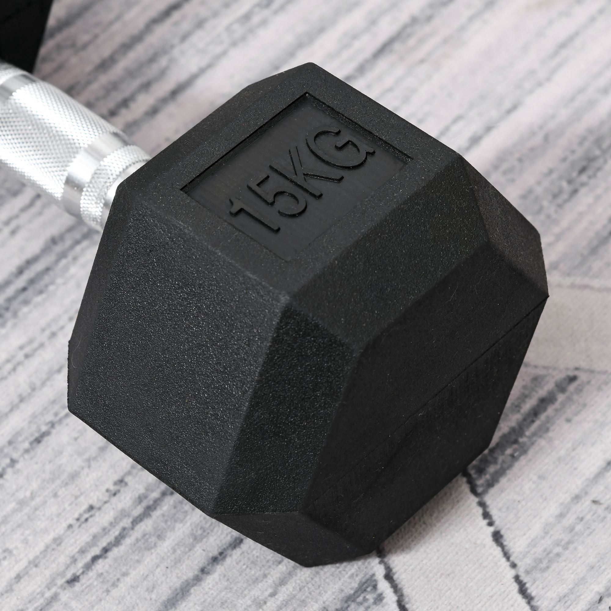Eine schwarze, sechseckige Hantel mit '15KG' auf dem Ende. Sie liegt auf einer strukturierten grauen Oberfläche.