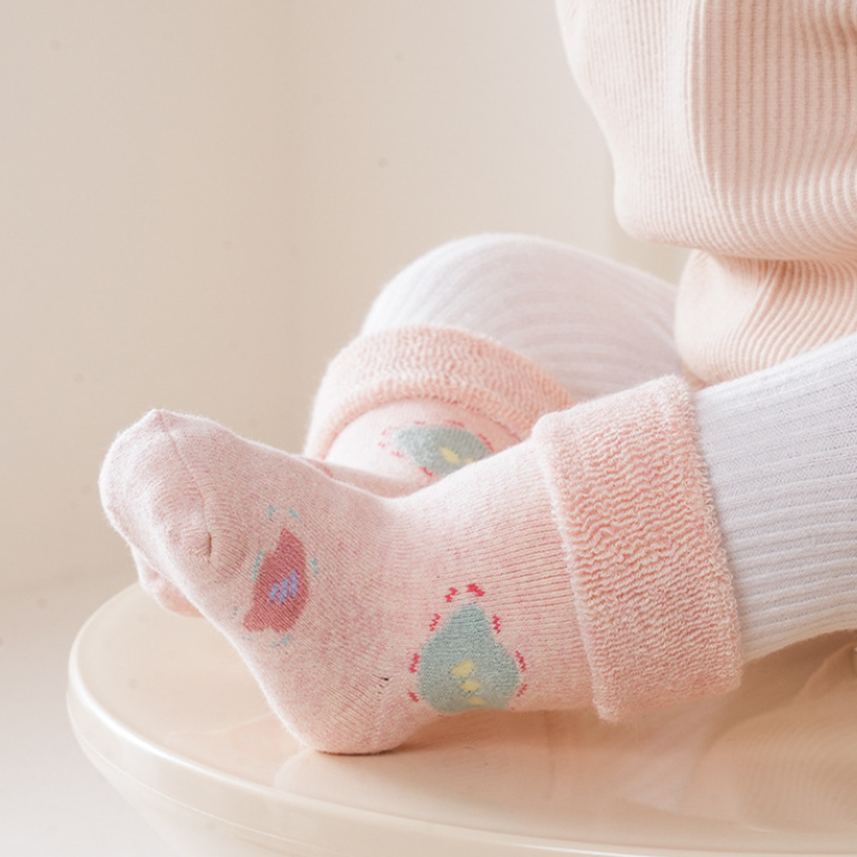 Babyfüße in rosa Socken mit Muster, ruhend auf einer cremefarbenen Oberfläche.