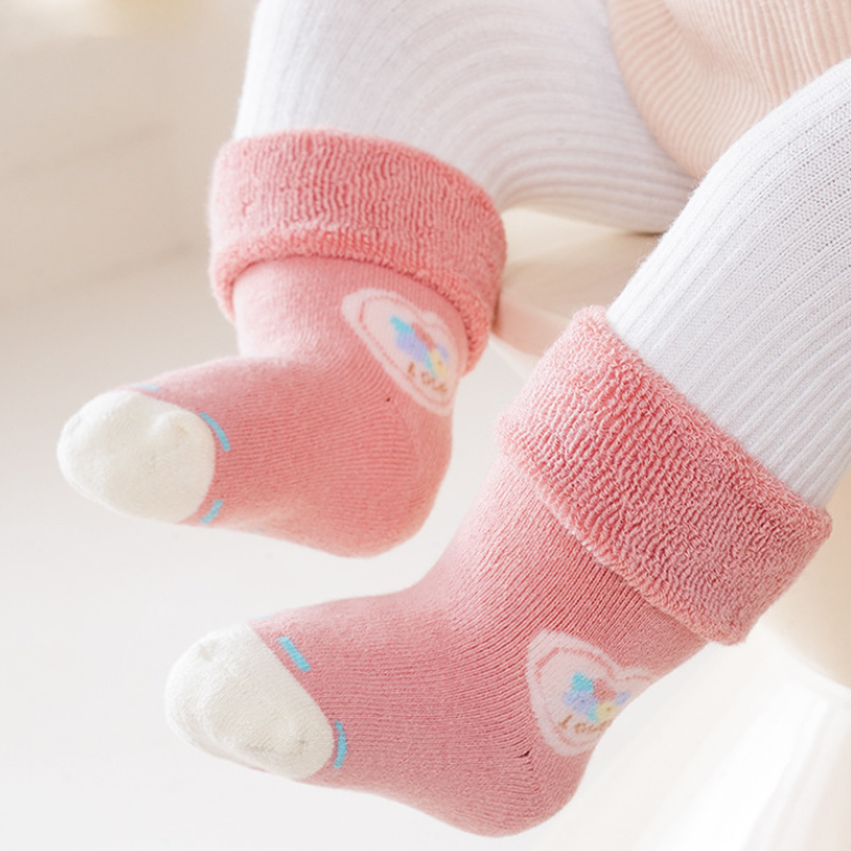 Babyfüße in rosa Socken mit Herzdesign. Weiße Leggings. Rosafarbene Manschette.