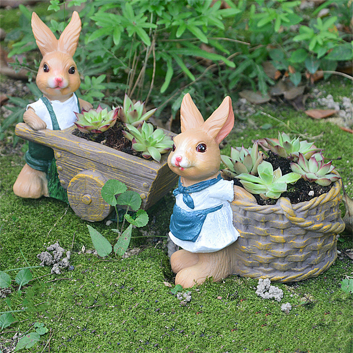 Hasenfiguren mit Pflanzgefäßen. Einer zieht einen Wagen, der andere hält einen Korb. Grünes Moos und Pflanzen im Hintergrund.