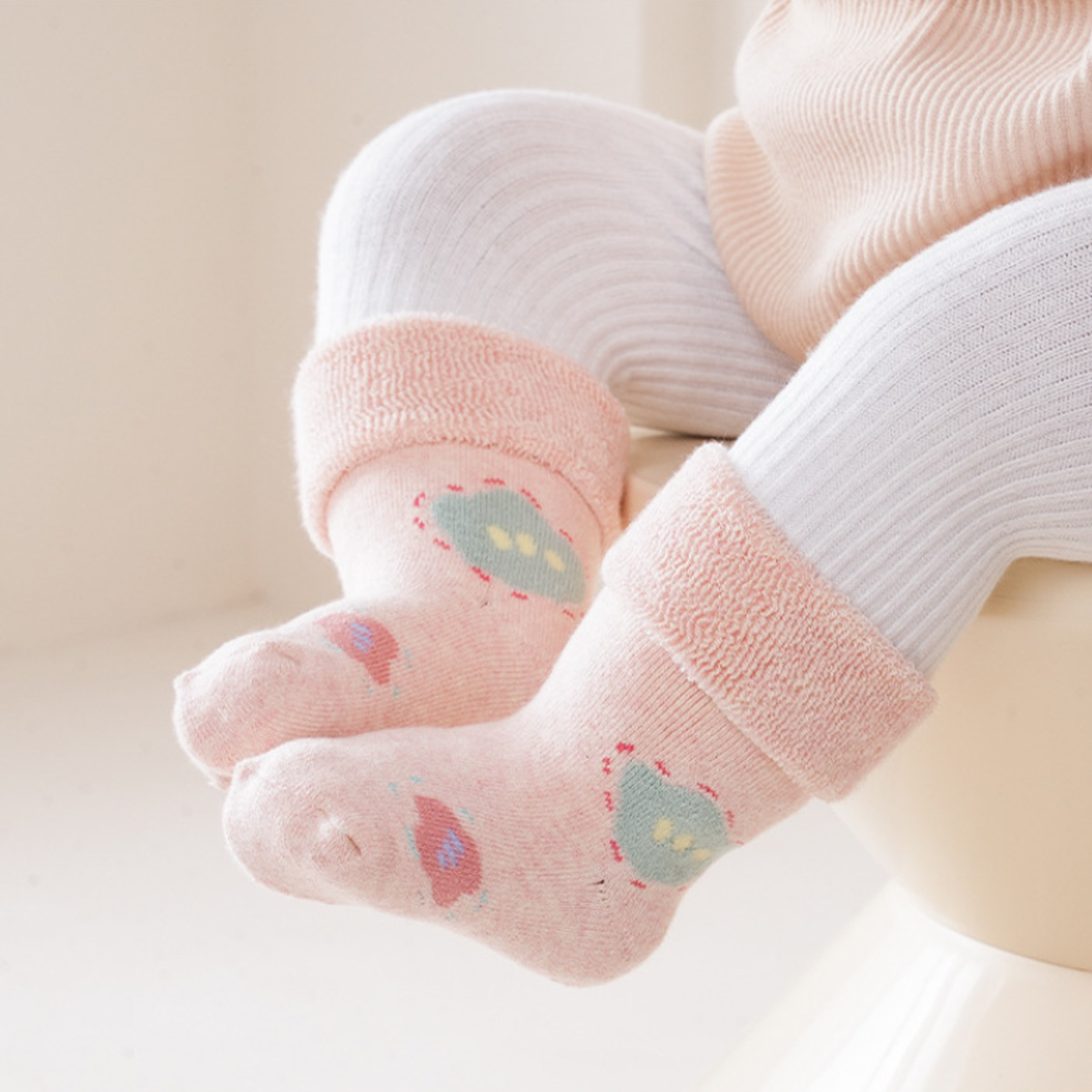 Babybeine mit rosa Socken mit grünen Designs und weißen Strumpfhosen. Cremefarbener Hintergrund.