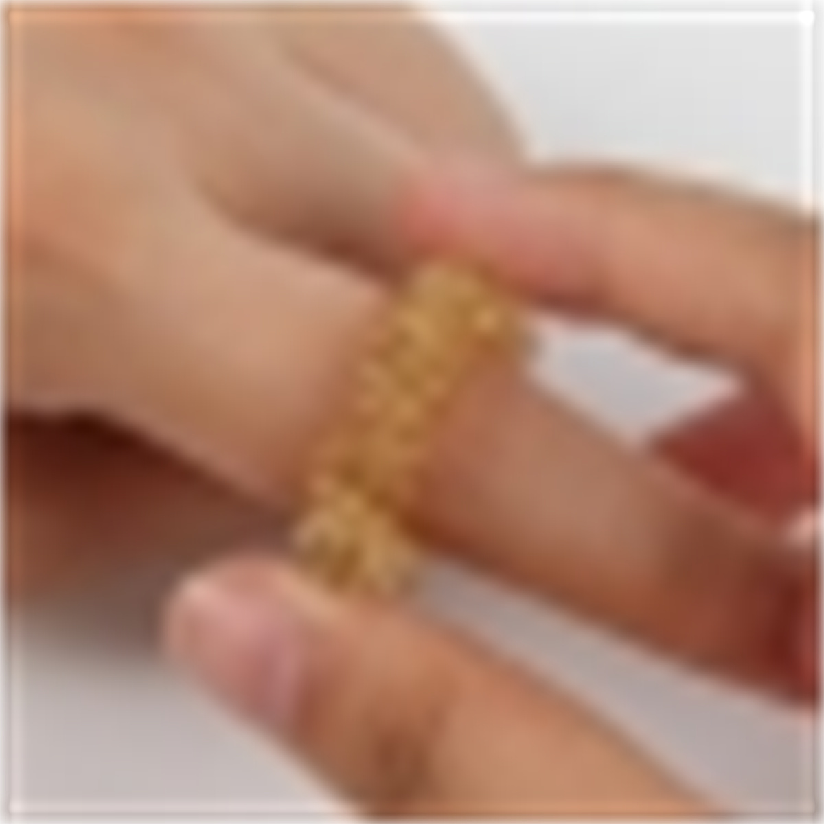 Ein goldfarbener Ring befindet sich an einem Finger, der von einer Hand berührt wird.