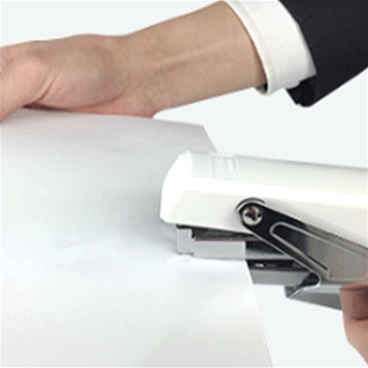 Eine Hand, die einen weißen Tacker auf weißem Papier verwendet, Nahaufnahme.