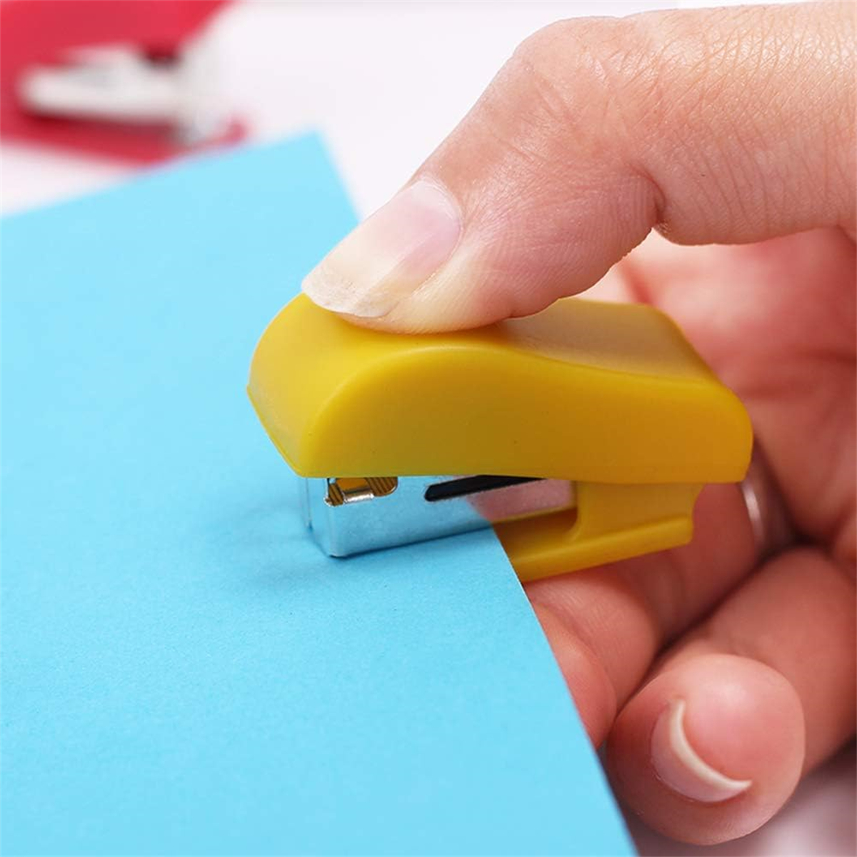 Ein gelber Tacker heftet ein blaues Blatt Papier zusammen. Der Tacker wird von einer Hand gehalten.