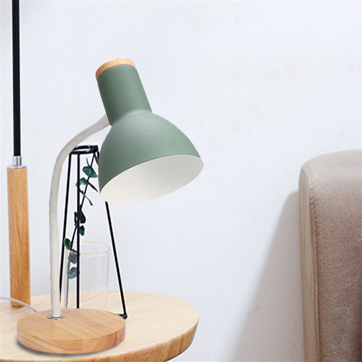 Grüne Schreibtischlampe auf einem Holztisch. Weißer Wandhintergrund. Die Lampe leuchtet.