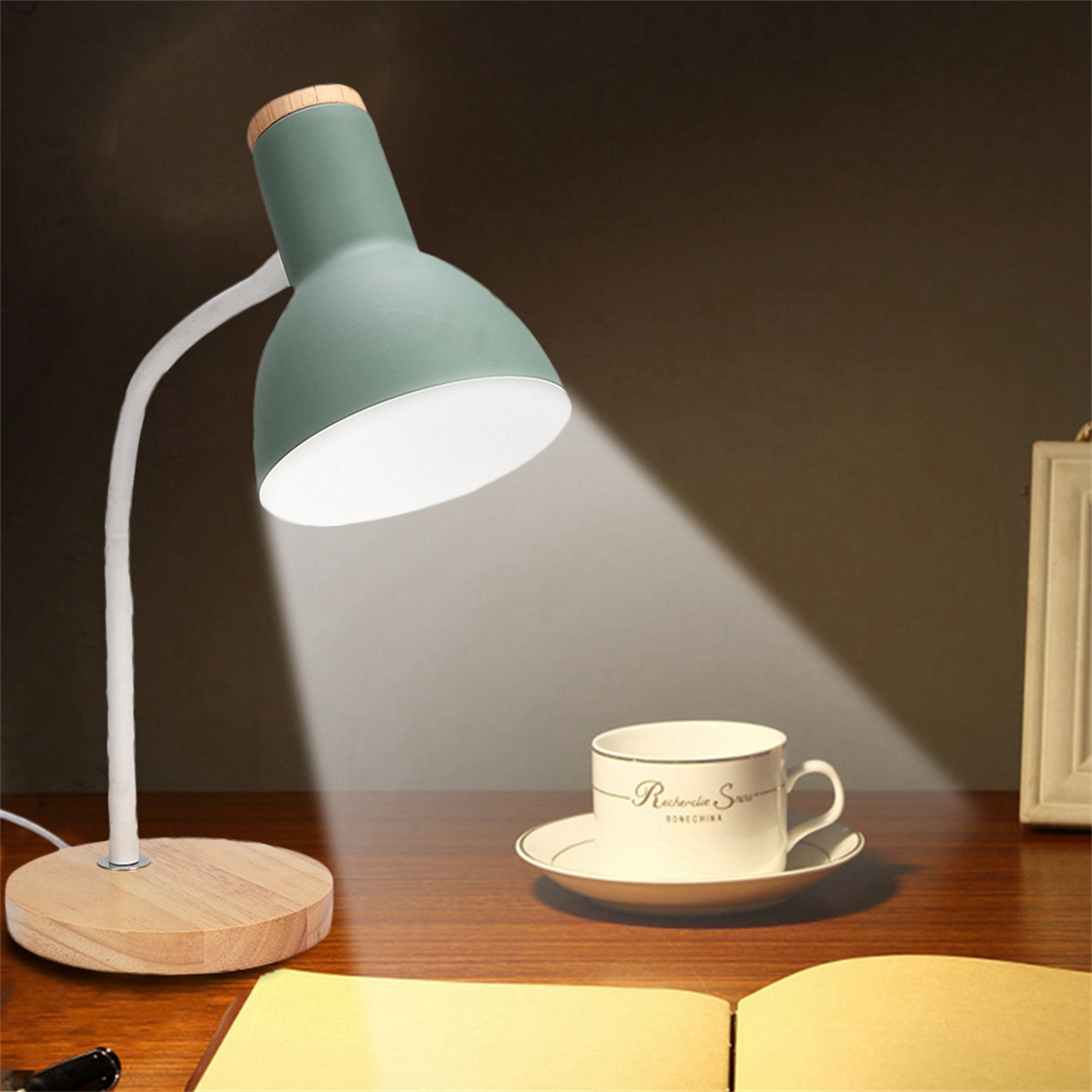 Grüne und Holz-Schreibtischlampe mit Tasse auf Untertasse und offenem Buch.