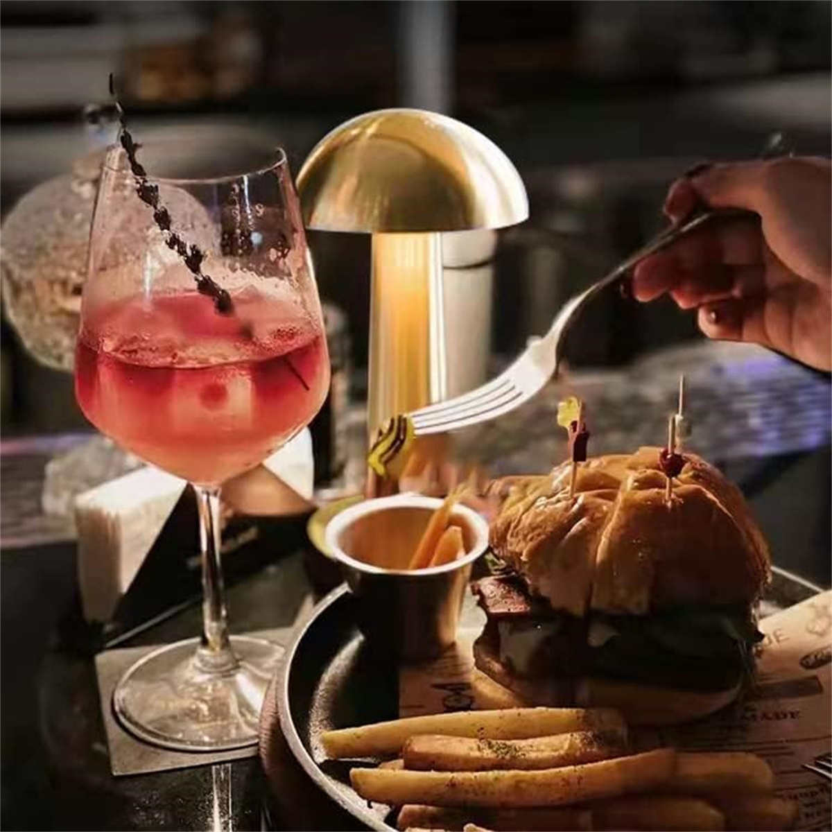 Tischarrangement mit Burger, Pommes und Getränk. Eine goldene Lampe beleuchtet die Szene.