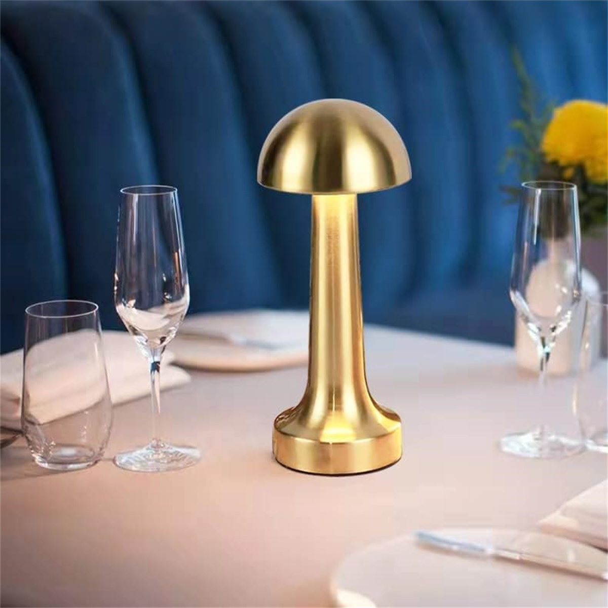 Goldene Tischlampe auf einem Tisch mit Weingläsern und blauer Wand im Hintergrund.