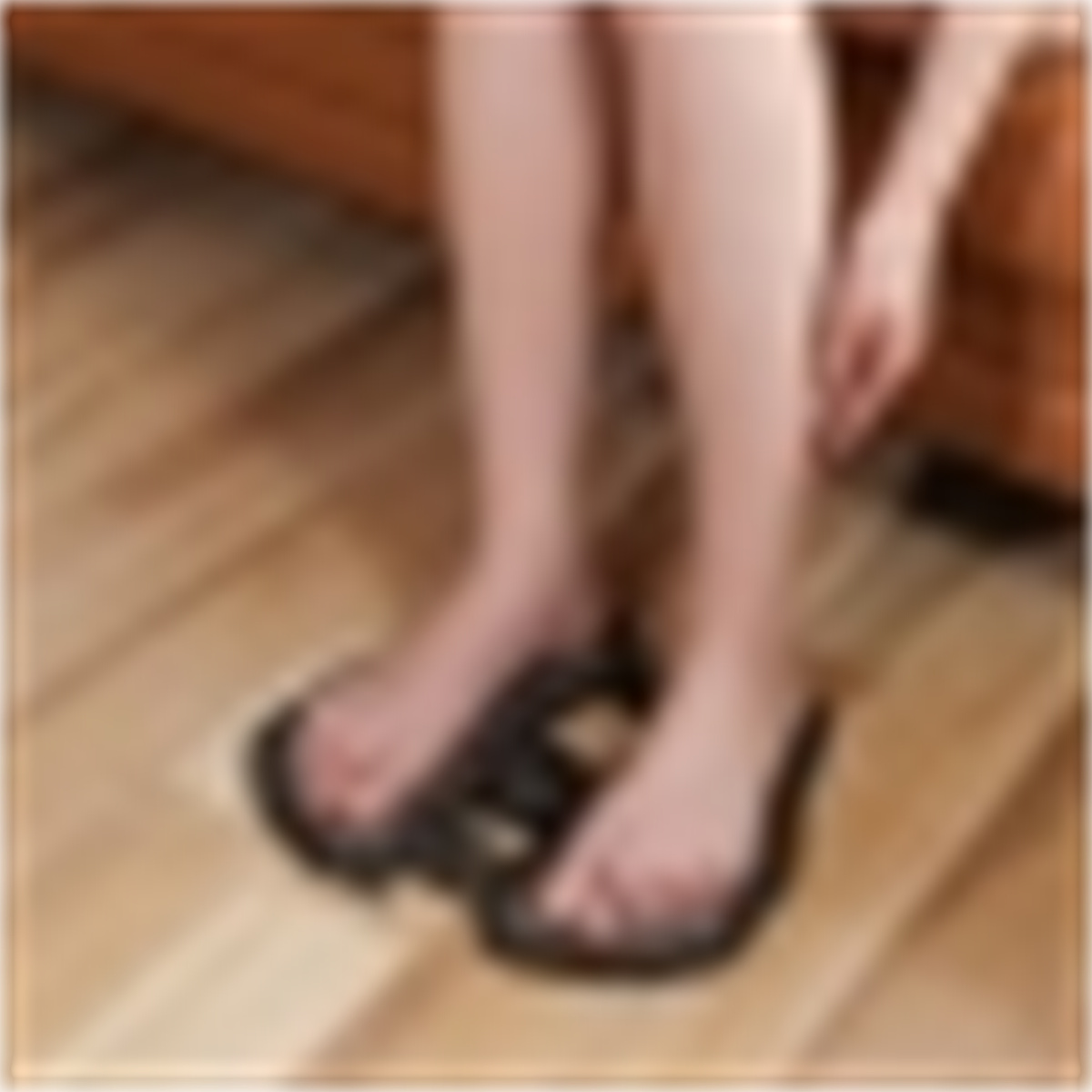 Die Füße einer Person in schwarzen Flip-Flops auf einem Holzboden, leicht unscharf.