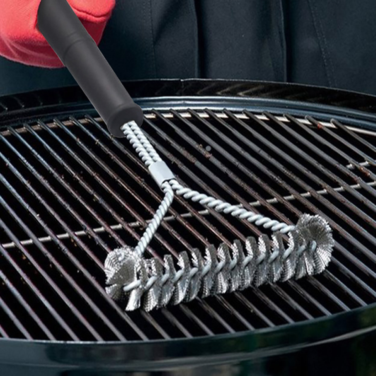 Eine Grillbürste mit schwarzem Griff reinigt einen Grill. Die Bürste hat Metallborsten.