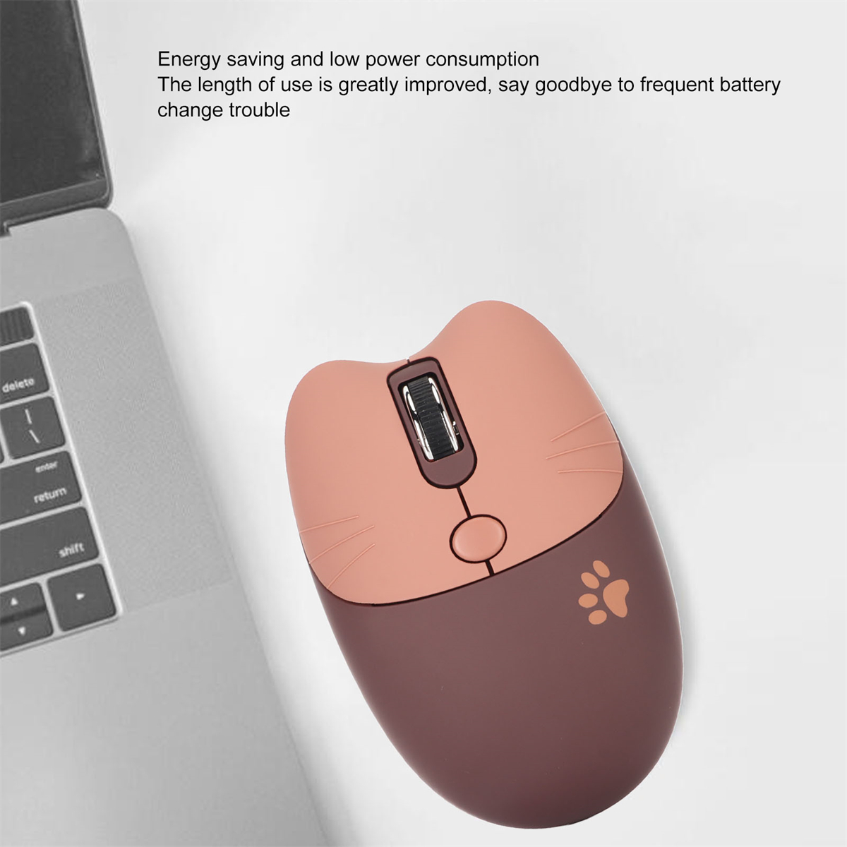 Eine rosa und braune katzenförmige kabellose Maus liegt auf einer weißen Oberfläche neben einer Laptop-Tastatur.