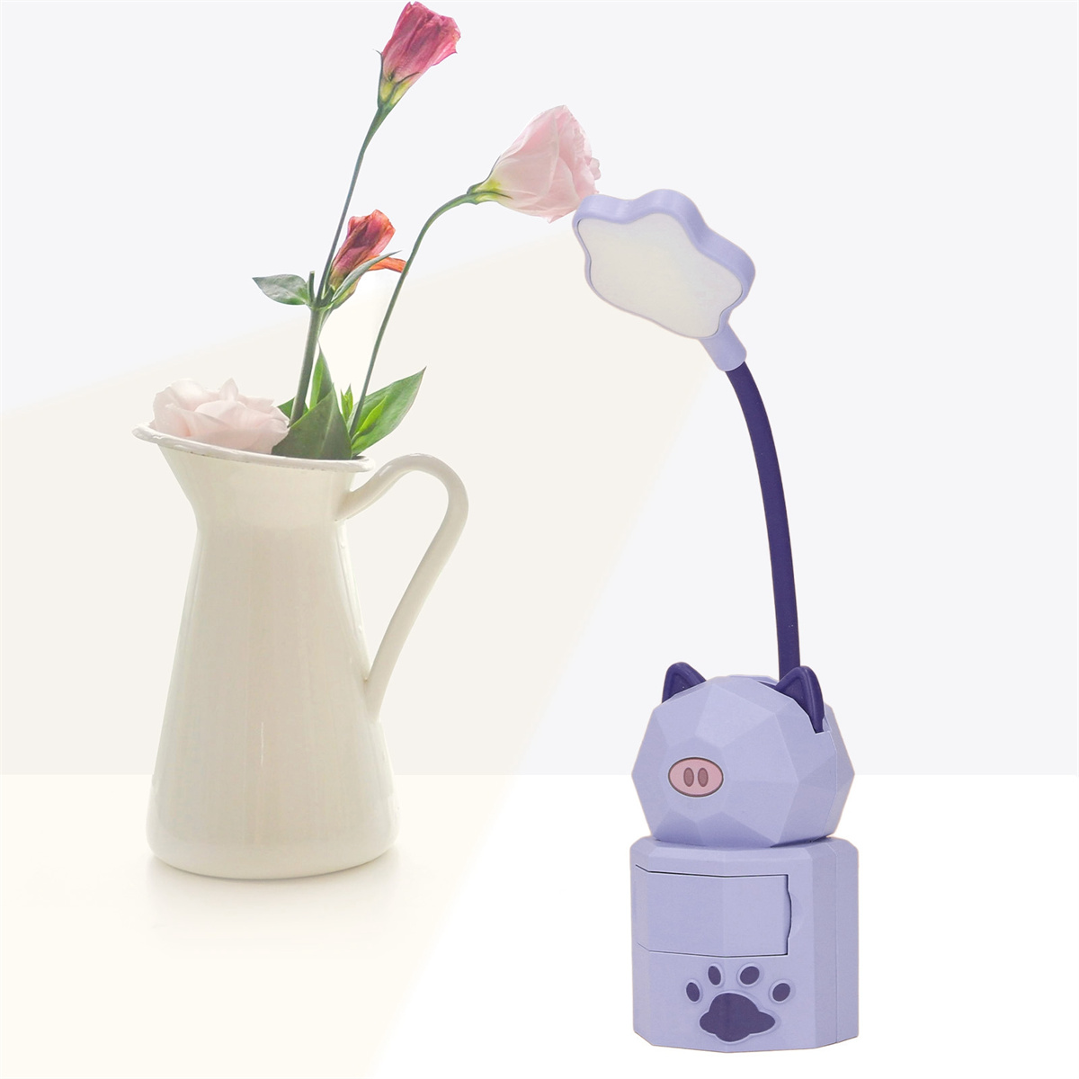 Eine schweineförmige Lampe mit lila Kopf, eine weiße Vase mit Blumen, auf weißer Oberfläche platziert.