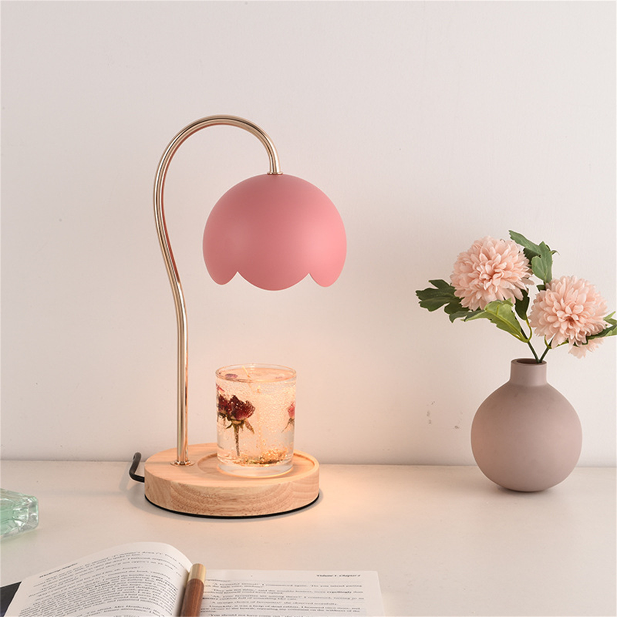 Eine rosa blütenförmige Lampe mit Holzsockel, einem Kerzenhalter und einer Vase mit Blumen.