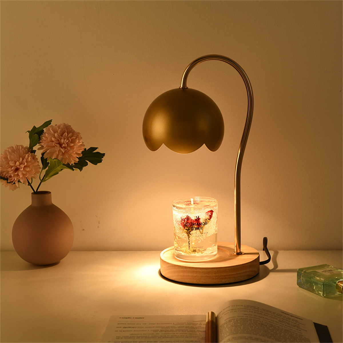Eine Tischlampe mit Kerze und Blumen auf einem Schreibtisch. Die Lampe hat einen goldenen Schirm.