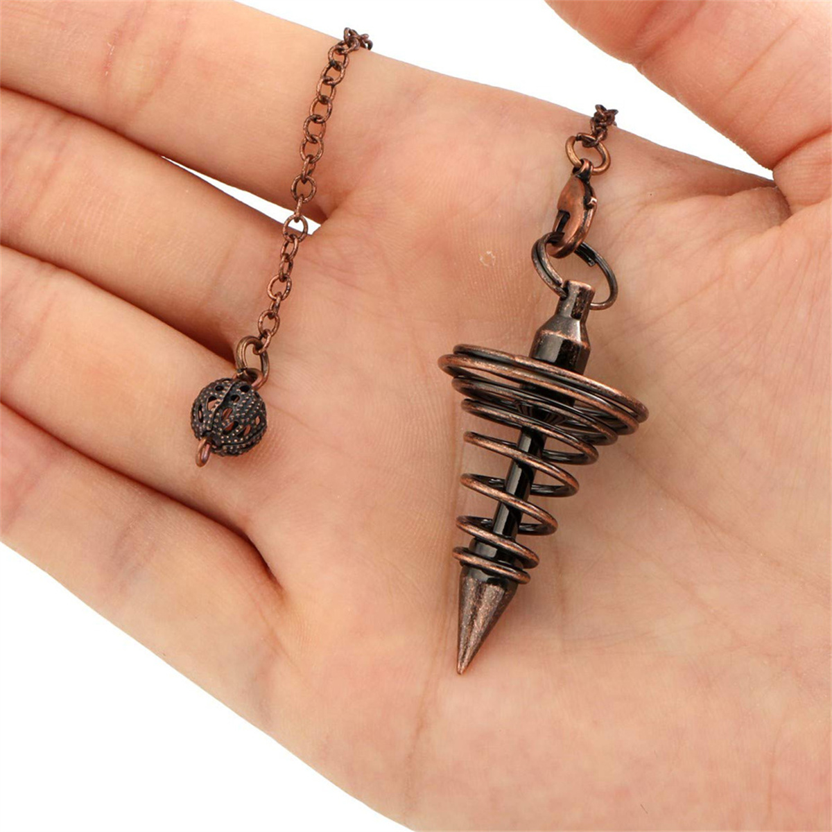 Nahaufnahme einer Hand, die ein Pendel mit kupferfarbenem Schmuck hält.