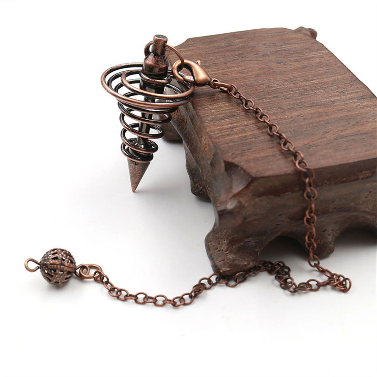 Ein kupferfarbenes Pendel, das an einem Holzblock hängt. Das Pendel hat ein Spiraldesign.