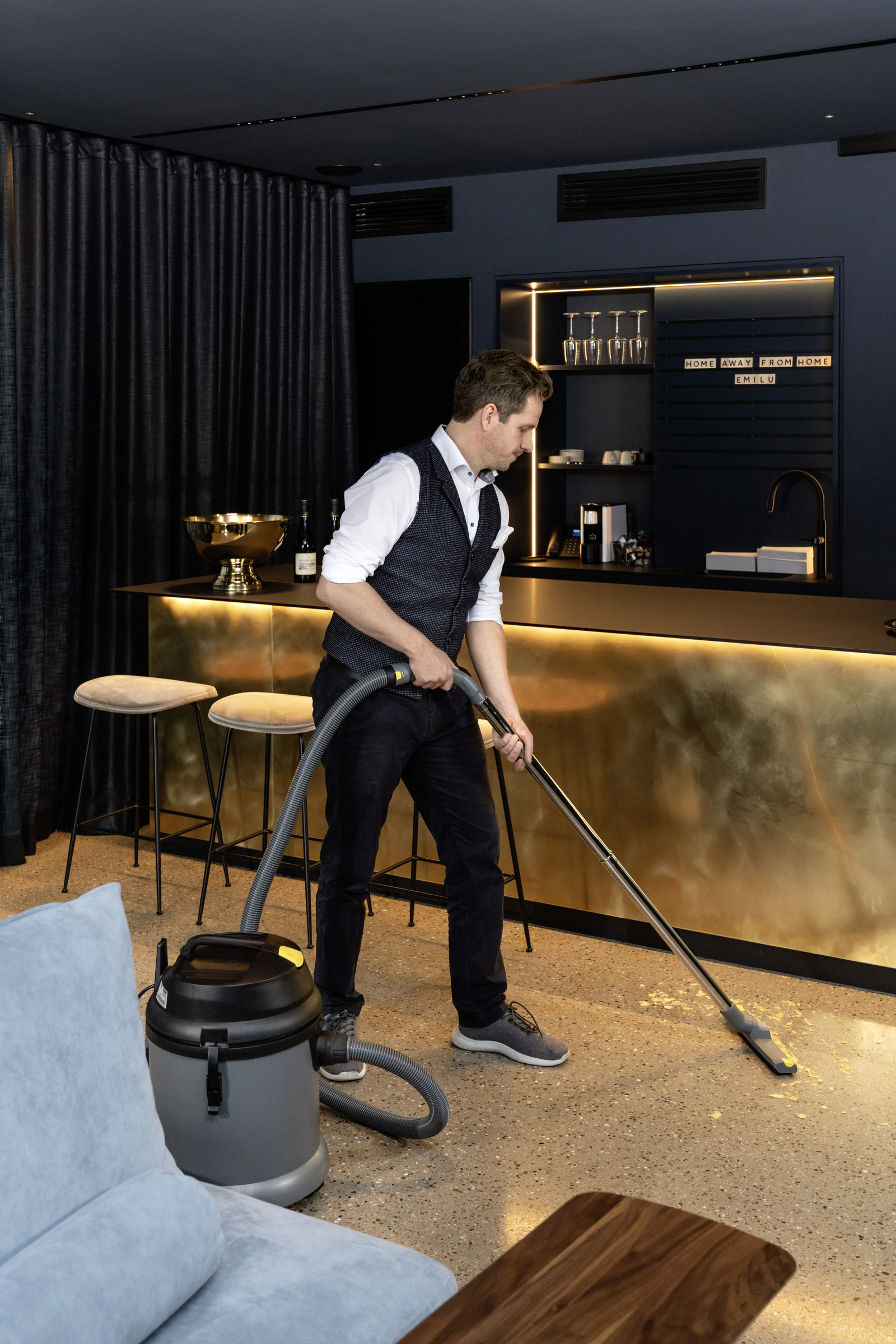 Un homme passant l'aspirateur dans une pièce avec un sol en bois franc, un bar doré et des murs bleu foncé.