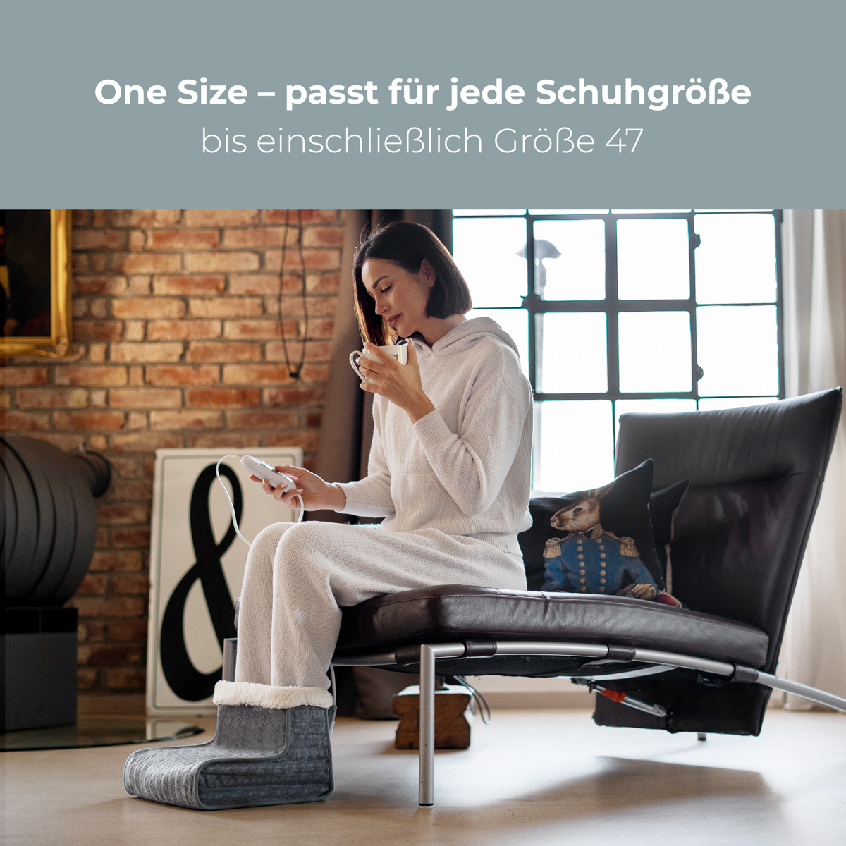 Kobieta w białej piżamie na czarnym krześle, w ogrzewaczu stóp, pije z kubka.