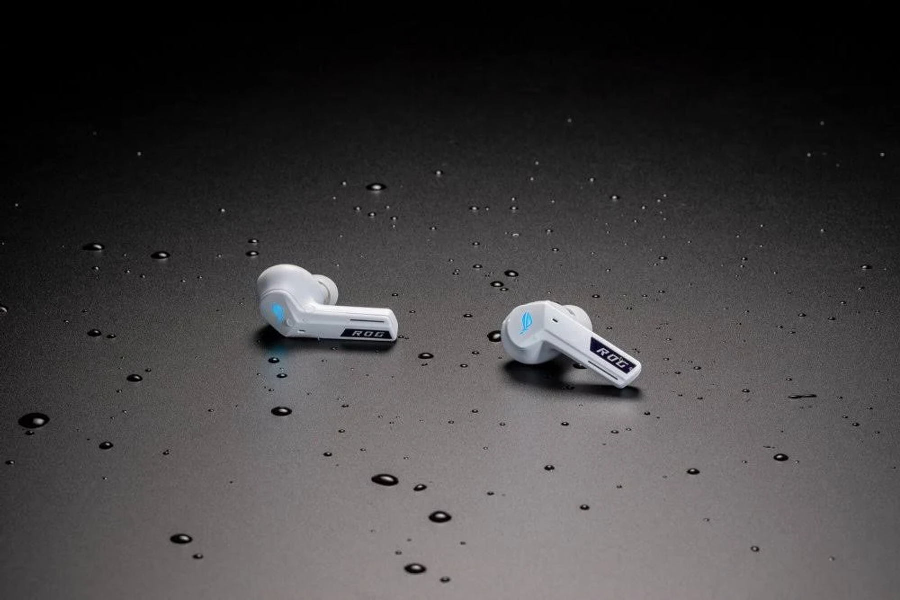 Due auricolari ROG bianche con accenti blu sono su una superficie scura e bagnata, con goccioline d'acqua.