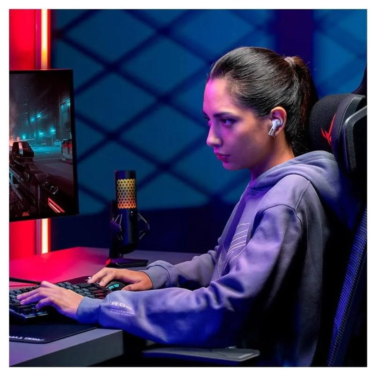 Una donna con auricolari e una felpa con cappuccio gioca a un tavolo con un computer e un microfono.