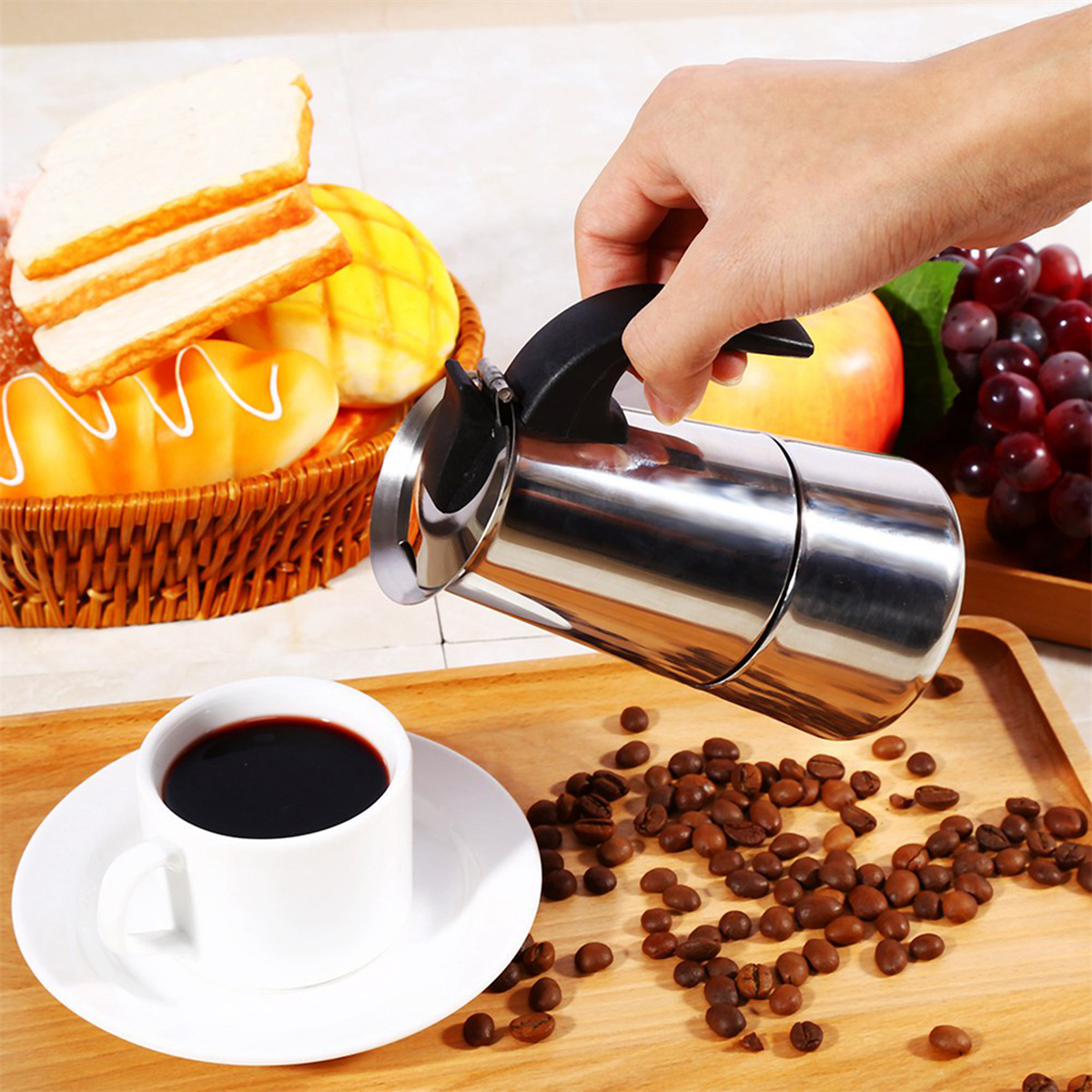 Eine Person gießt Kaffee aus einem verchromten Moka-Kocher in eine weiße Tasse auf einer Untertasse mit Bohnen.