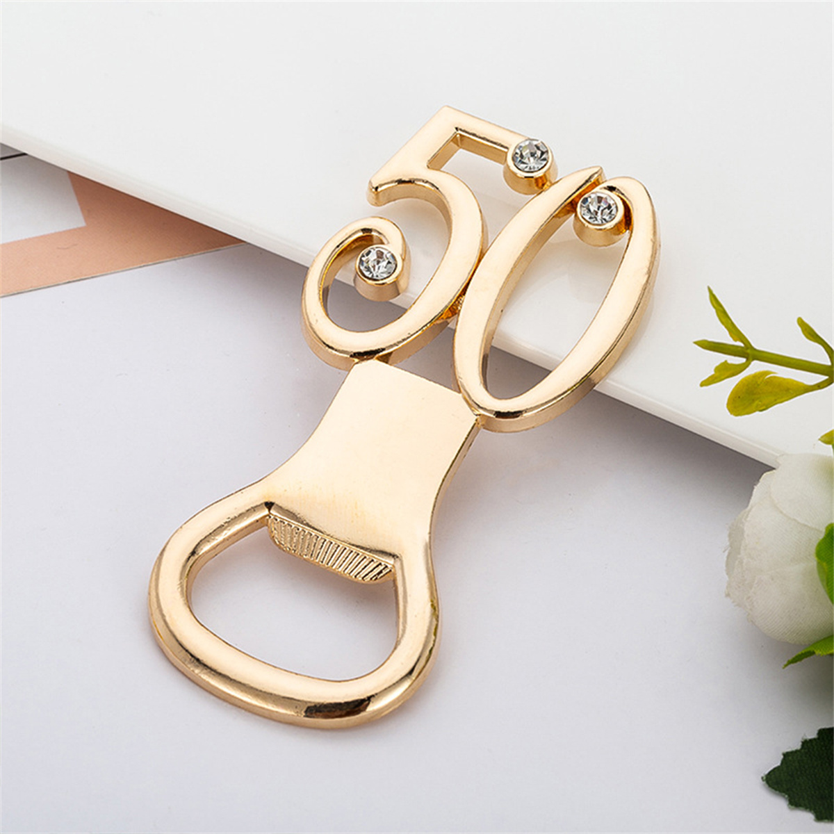 Goldener Flaschenöffner in Form einer '50' mit Diamanten. Auf weißer Oberfläche.