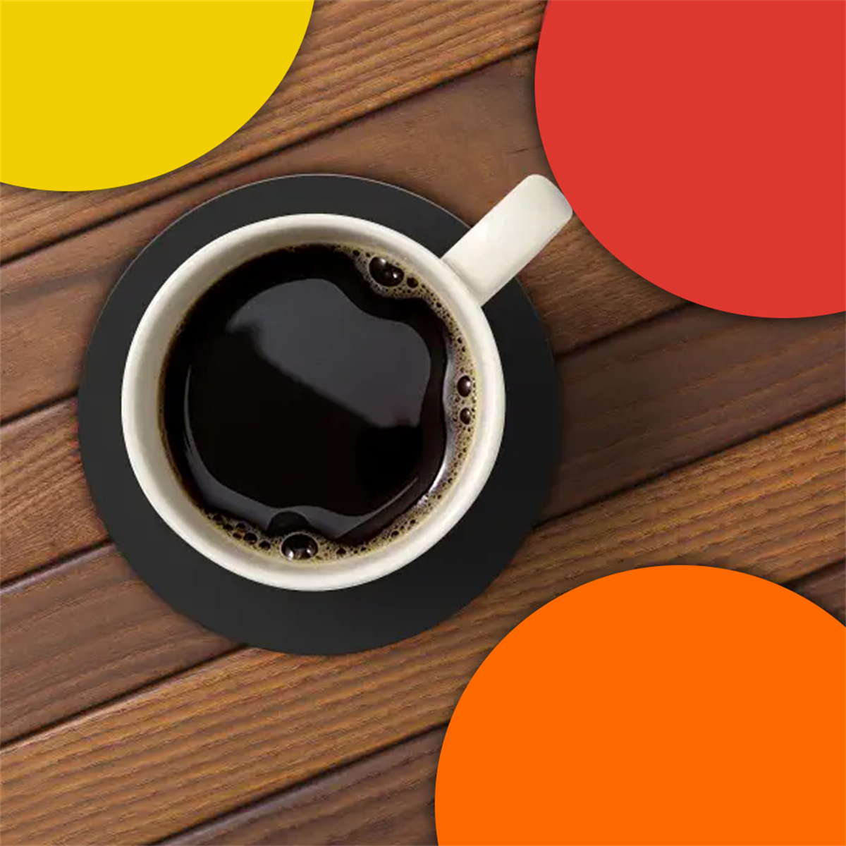 Kaffee in weißer Tasse auf schwarzem Untersetzer. Holztisch mit gelbem, rotem und orangenem Hintergrund.