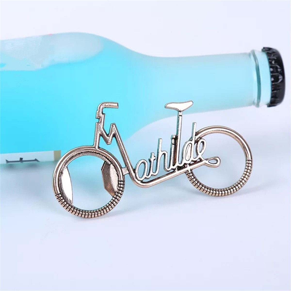 Ein flaschenöffner in Form eines Fahrrades mit dem Namen 'Mathilde' und einer blauen Flasche.