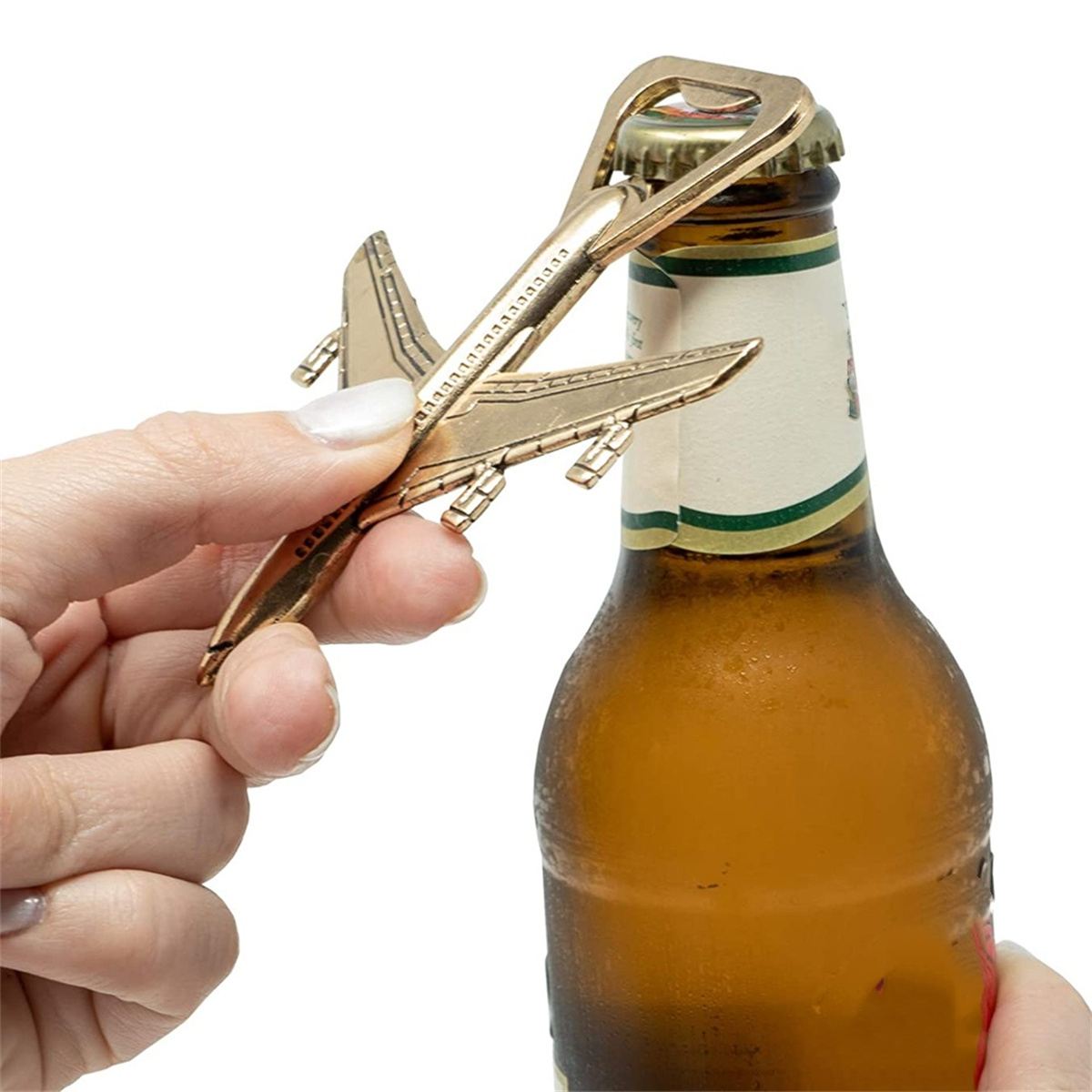 Eine Hand öffnet eine Bierflasche mit einem goldenen flugzeugförmigen Flaschenöffner. Bierflasche ist bernsteinfarben.