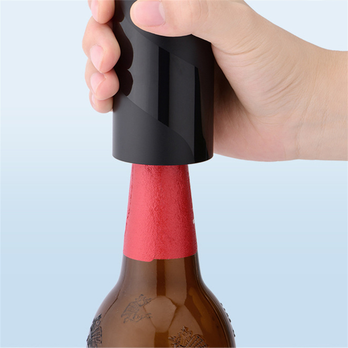 Eine Hand, die einen schwarzen Flaschenöffner auf einer braunen Flasche mit rotem Hals benutzt.