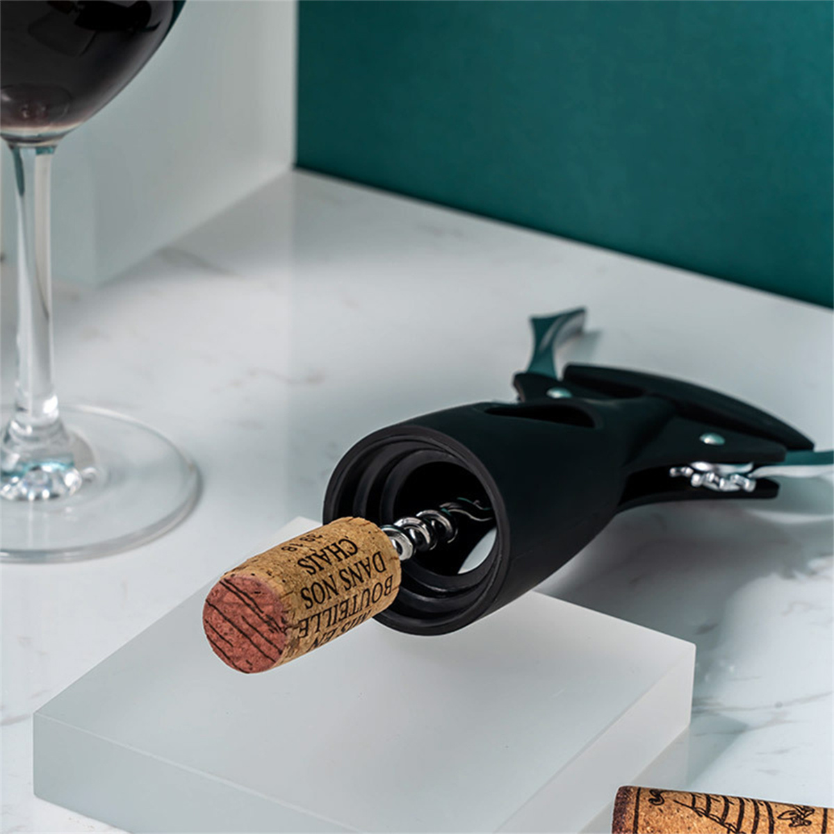 Korkenzieher entfernt einen Korken aus einer Flasche, im Hintergrund ein Glas Rotwein.