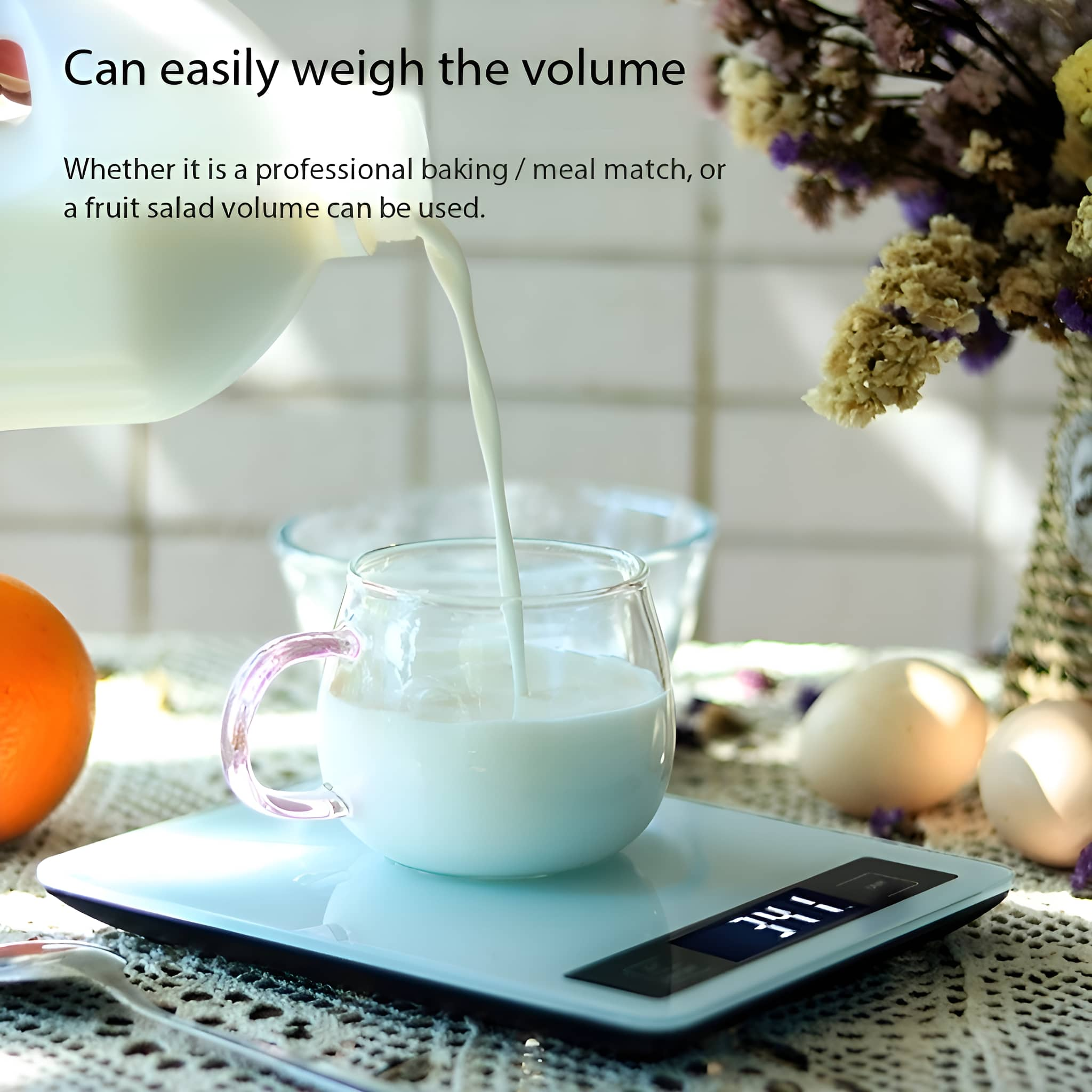 Milch wird in ein Glas auf einer Waage gegossen. Eier und Blumen im Hintergrund.