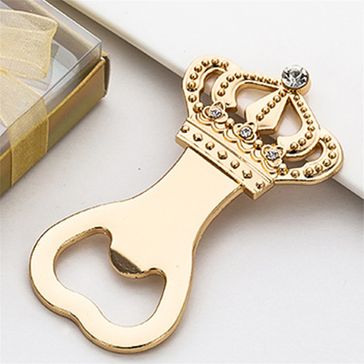 Goldener kronenförmiger Flaschenöffner mit Strasssteinen auf weißer Oberfläche.