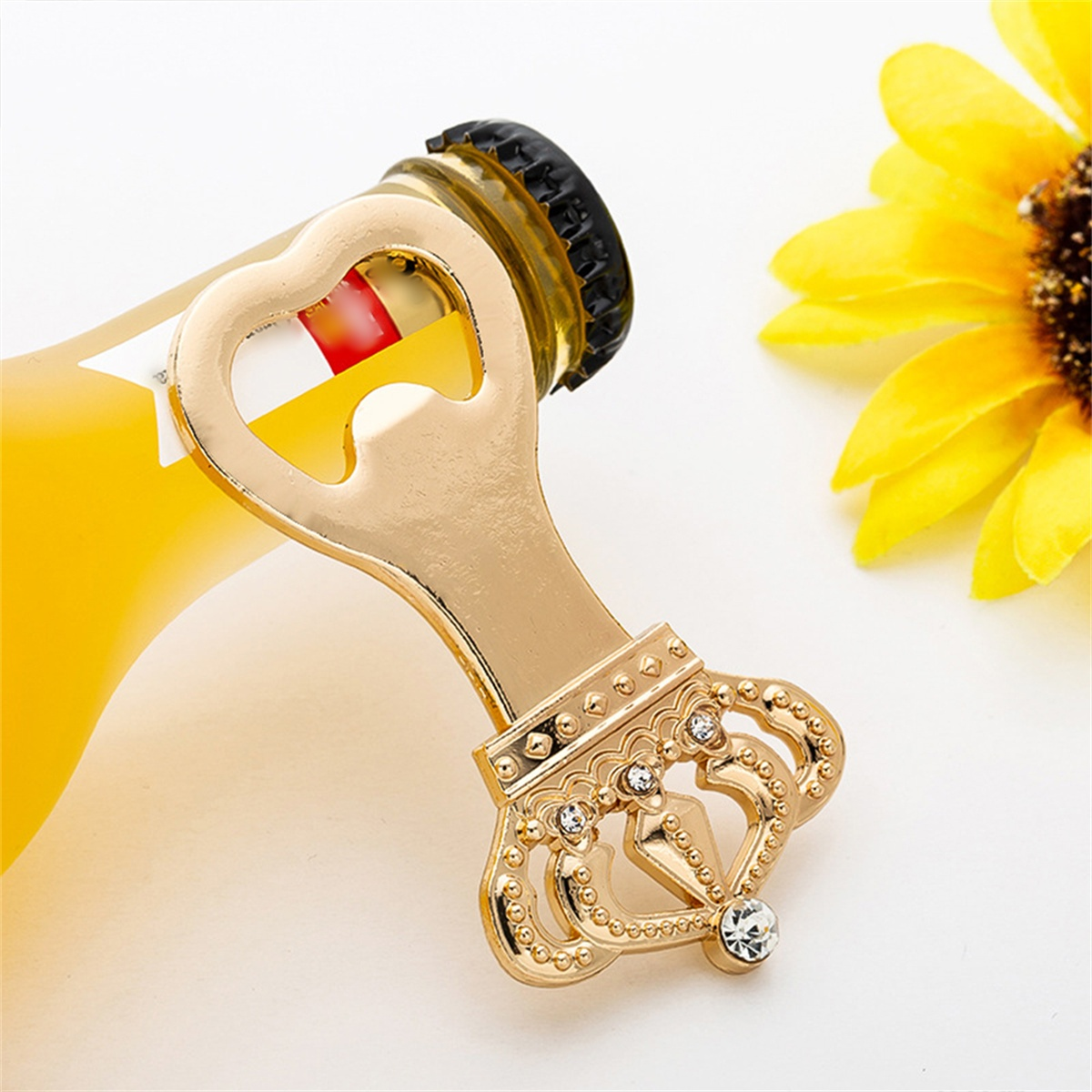 Ein goldener Flaschenöffner mit Kronen-Design und eine Bierflasche. Eine gelbe Sonnenblume im Hintergrund.