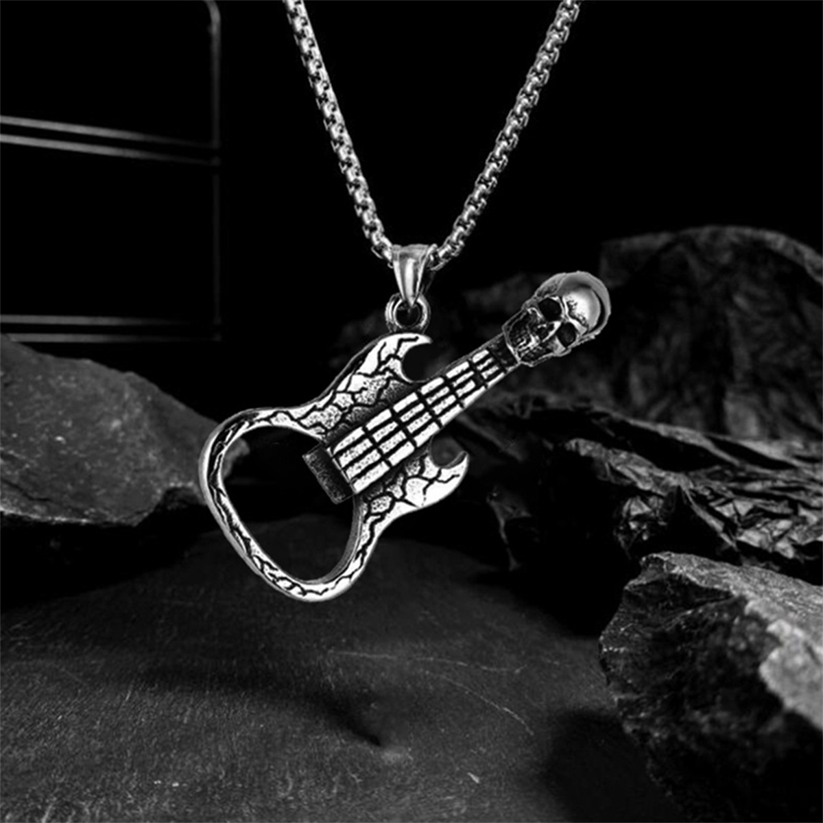 Silberner Gitarrenanhänger mit Totenkopf oben. Auf einer Kette, vor dunklem Hintergrund.