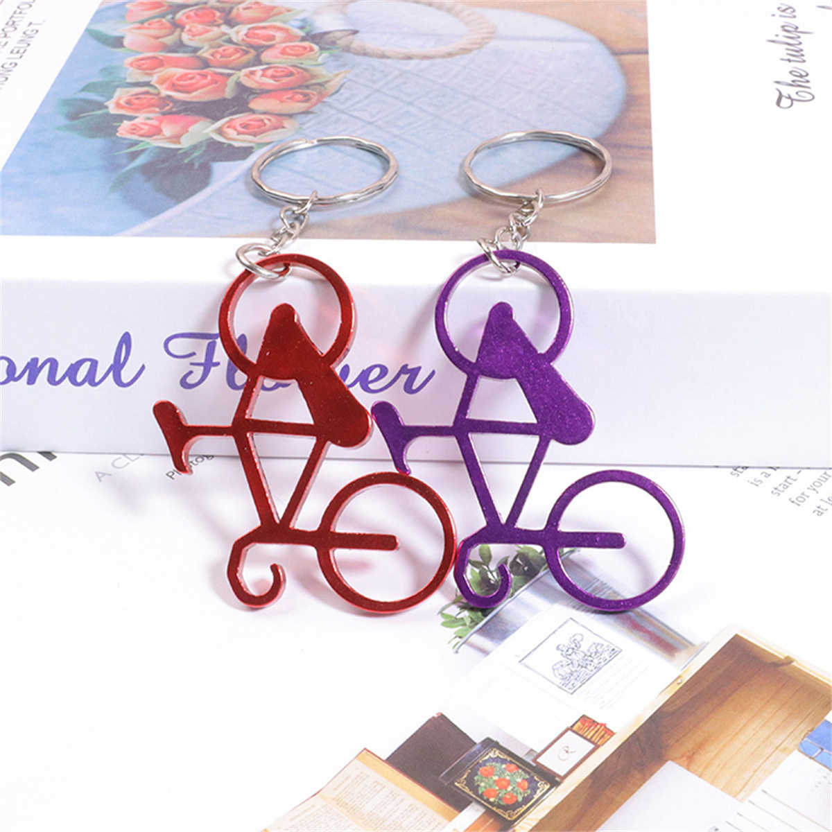 Zwei Fahrrad-Schlüsselanhänger, rot und lila, hängen über einer Seite mit Text und Blumenhintergrund.