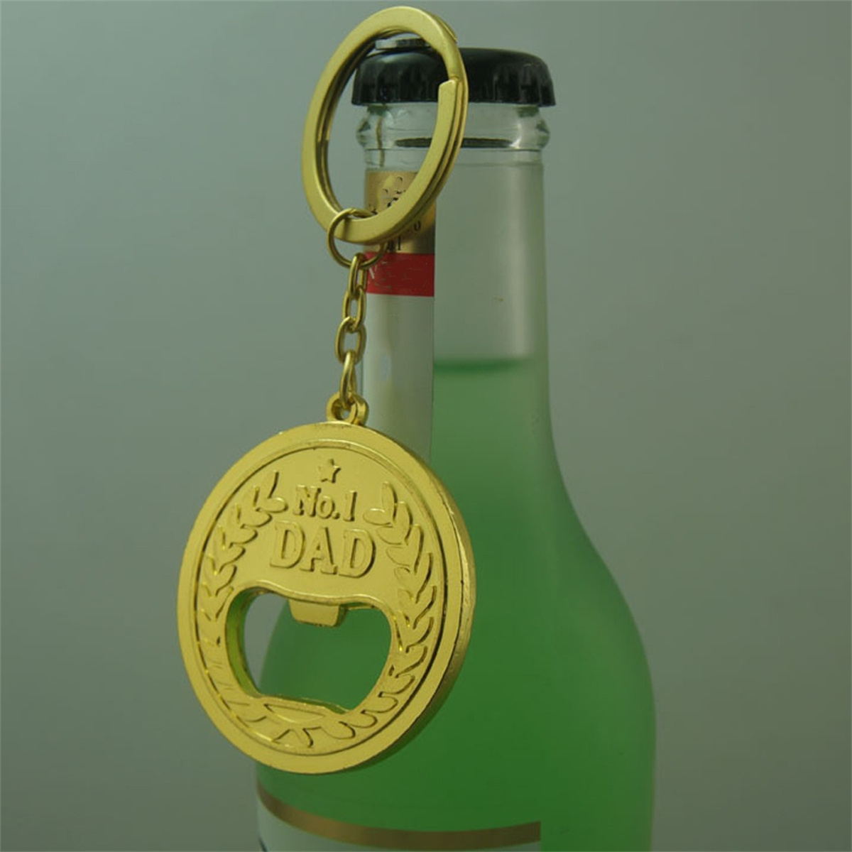 Ein goldener Flaschenöffner-Schlüsselanhänger in Form einer Medaille mit einer Flasche dahinter.
