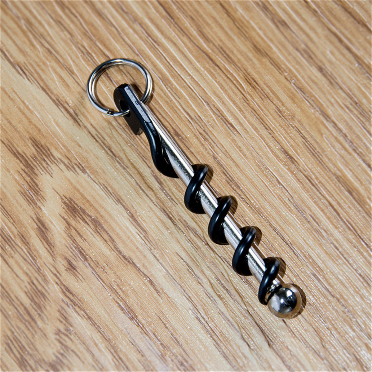 Ein Korkenzieher auf Holzmaserung. Er hat eine Silberschraube, schwarze Spiralen und einen Ring.